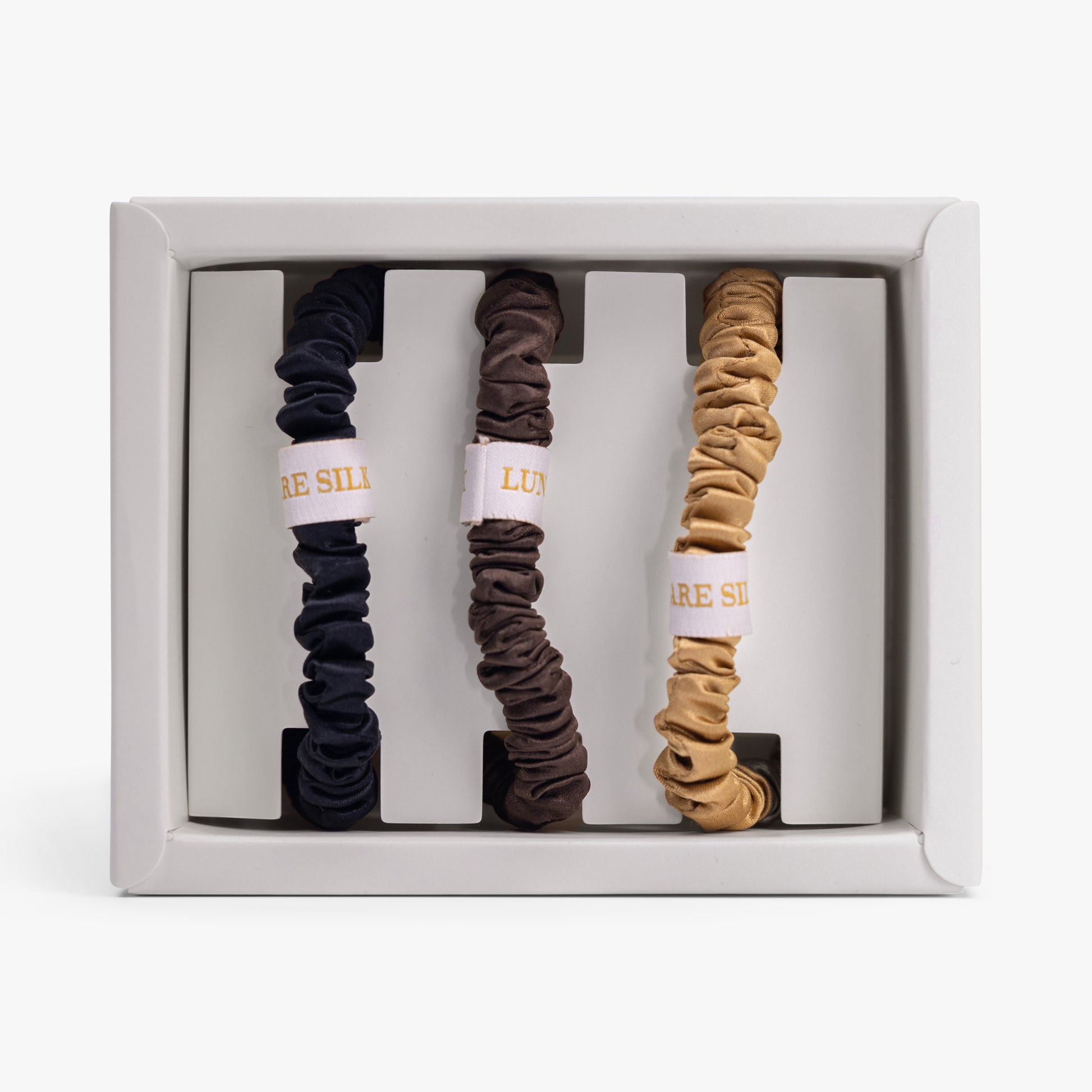 Set of three scrunchies in black, brown, and beige with visible brand name in a box.