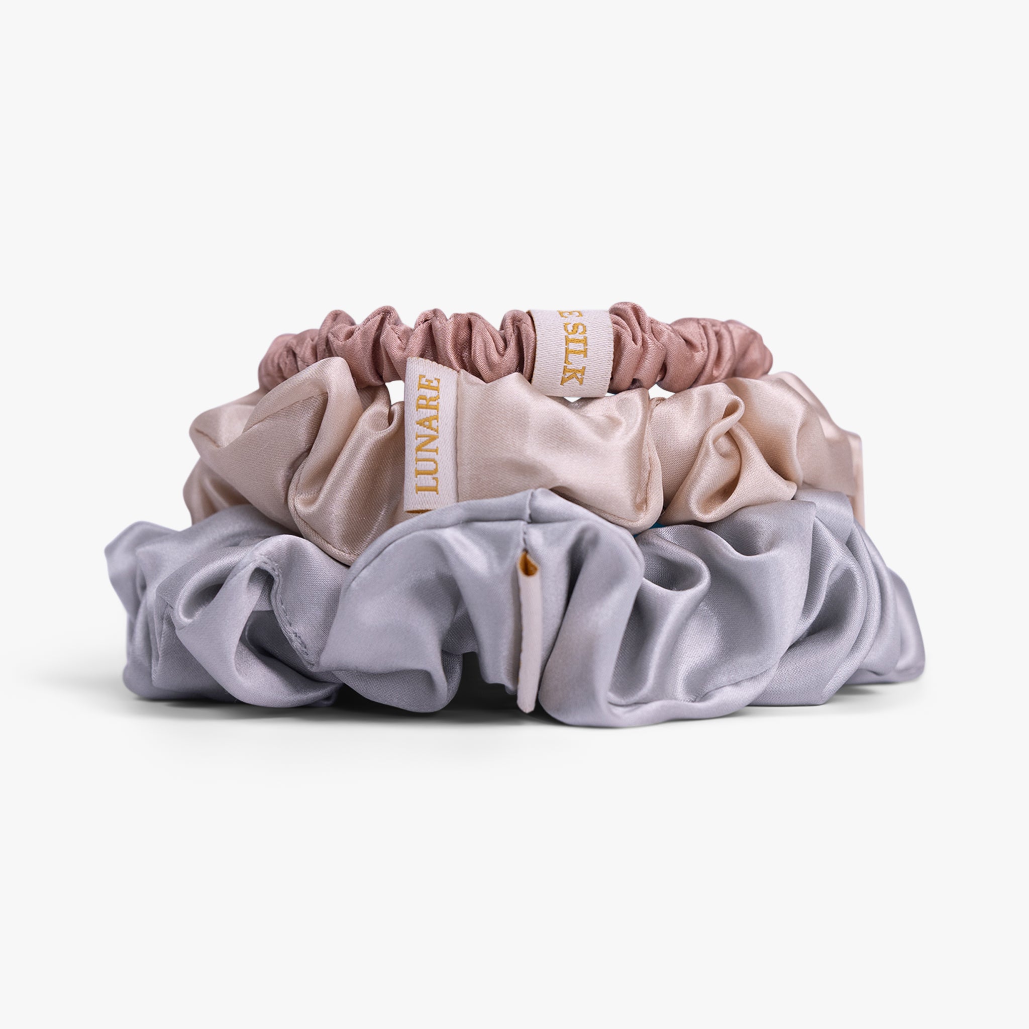 Set of three scrunchies in pink, beige, and gray on a white background