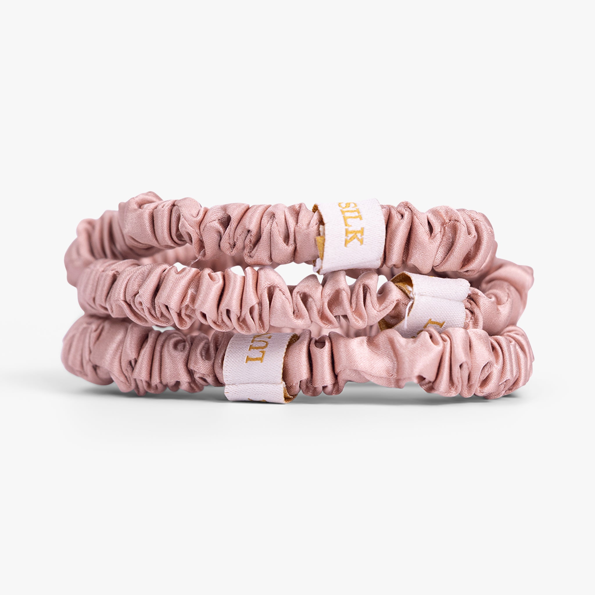 Rose gold silk scrunchies stacked on white background
