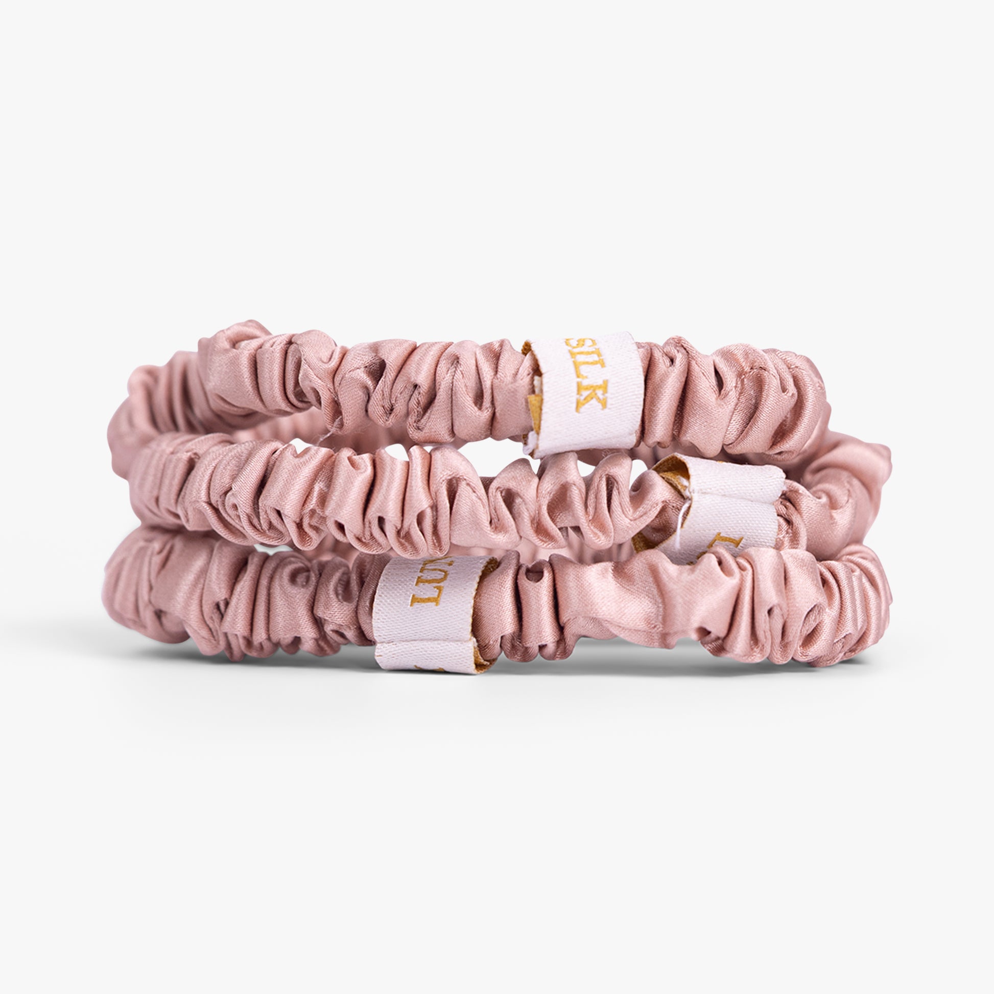 Rose gold silk scrunchies stacked on white background
