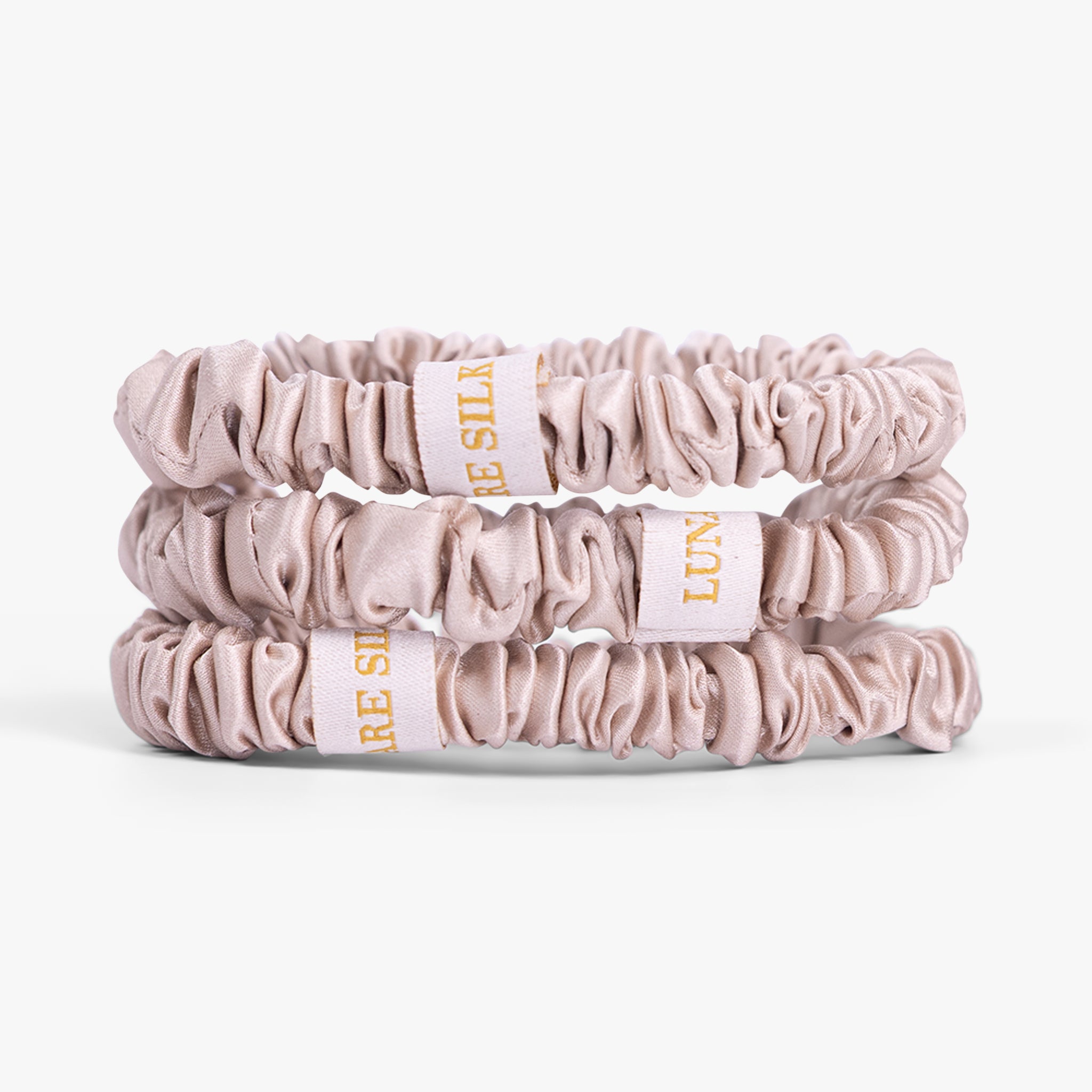 Three champagne scrunchies with visible branding on a white background