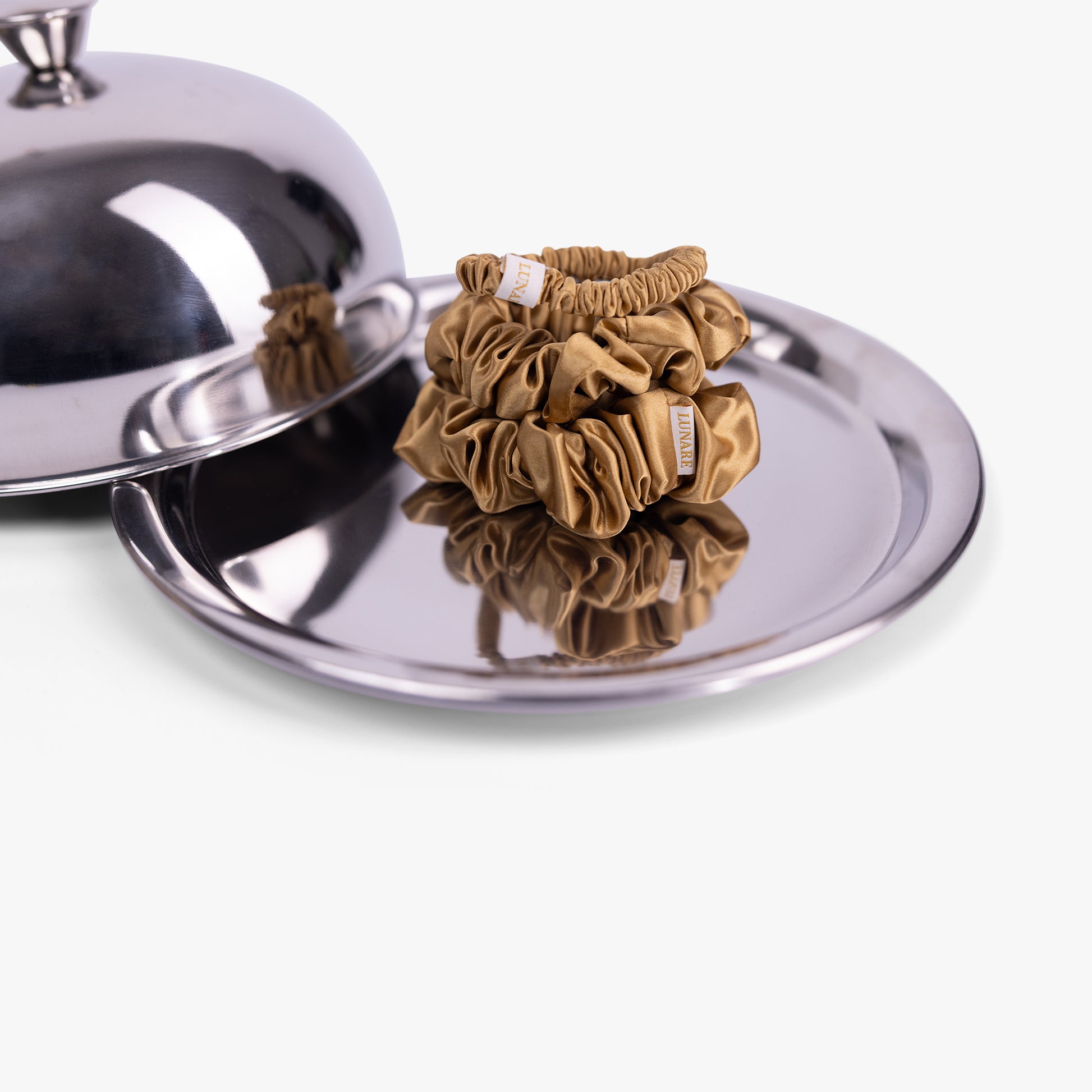 Amber gold silk scrunchies on silver tray with lid
